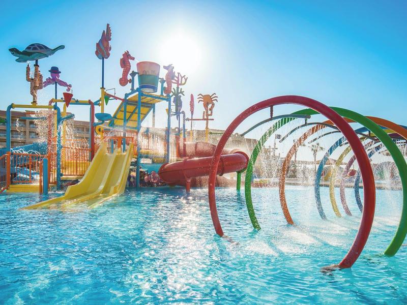 Colorful water park with slides and rings over a pool under bright sunlight.