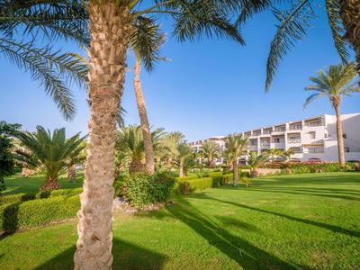 Hotel building with well-maintained garden and palm trees under clear blue sky.
