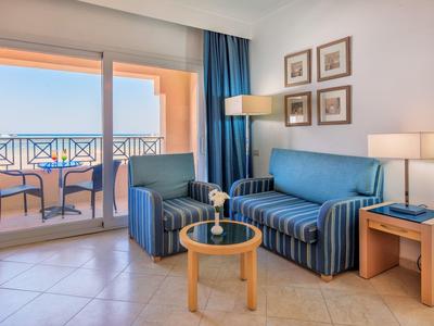 Bright living room with blue sofa, table, and balcony overlooking the sea.