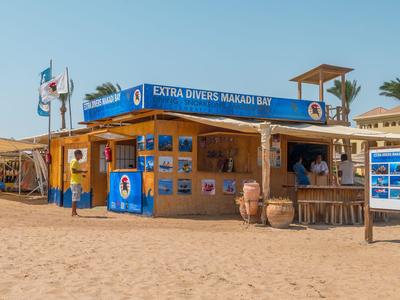 Kleiner Verkaufsstand am Strand mit blauer Beschilderung und Palmen im Hintergrund.