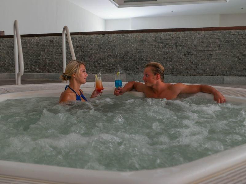 A couple relaxing in a hot tub, toasting with cocktails.