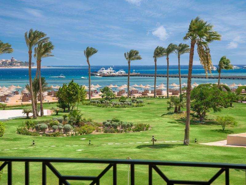 View of a tropical garden with palm trees and ocean in the background.