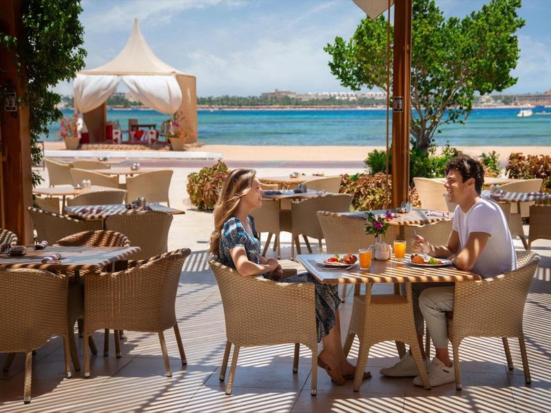 Two women sit at an outdoor table overlooking the beach and sea.