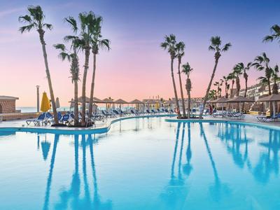 Una grande piscina dell'hotel con palme e lettini al tramonto.