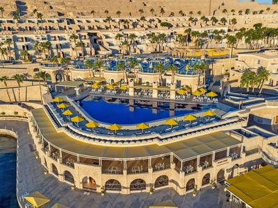 Hotel di lusso con grandi piscine e lettini in un paesaggio desertico soleggiato.