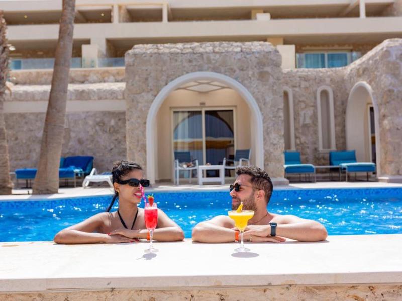 Couple with colorful cocktails relaxing in a hotel pool with stone walls and palm trees.