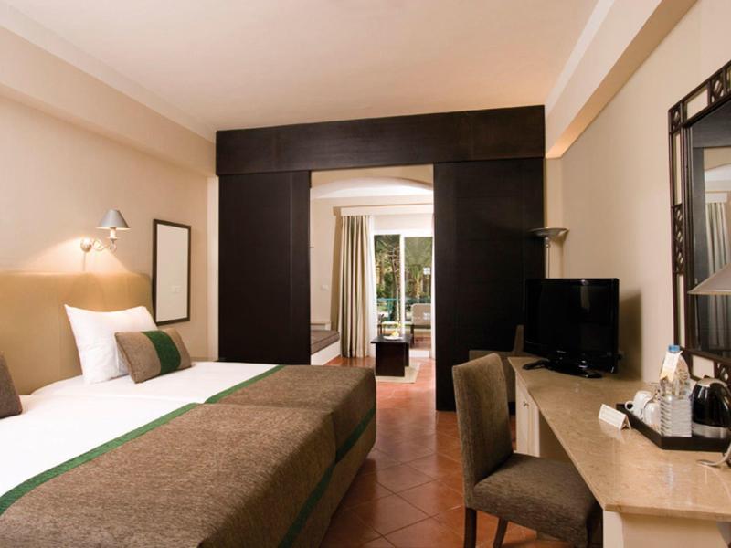 Modern hotel room with large bed, desk, TV, and view of the terrace.