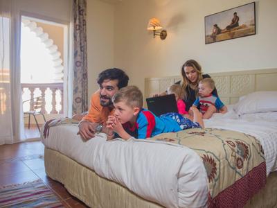 Rodzina z dwójką dzieci odpoczywa razem na łóżku w jasnym pokoju hotelowym.