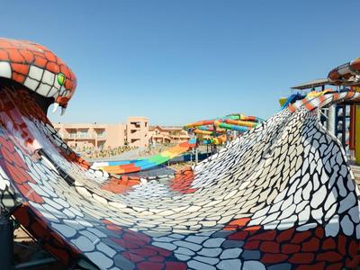Tobogán de agua ondulado con patrón de escamas coloridas en un parque acuático bajo cielo despejado.
