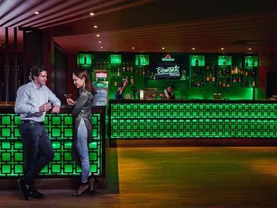 Deux personnes discutent au bar éclairé en vert dans un espace élégant d'hôtel ou de lounge.