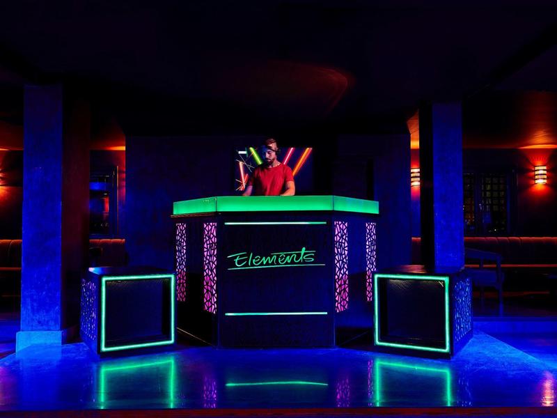 Neon-lit DJ booth in a dark club with a person holding up peace signs.