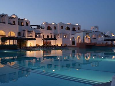 Abendaufnahme eines Hotels mit beleuchtetem Pool und weißer mediterraner Architektur