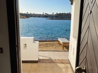 Blick durch eine offene Tür auf eine Terrasse mit Meerblick und klarem Himmel.