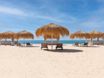 Beach chairs under straw umbrellas on a sandy beach with a clear blue sky