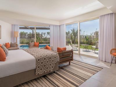 Bright hotel room with king bed, patterned linens, orange accents, and sliding glass doors to balcony.