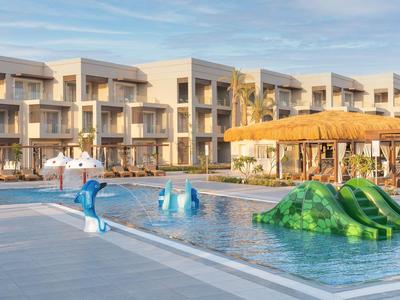 Resort pool with water slides and dolphin fountains in front of modern hotel buildings.