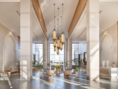 Bright hotel lobby with high ceilings, modern hanging lights, and wooden fabric seating areas.