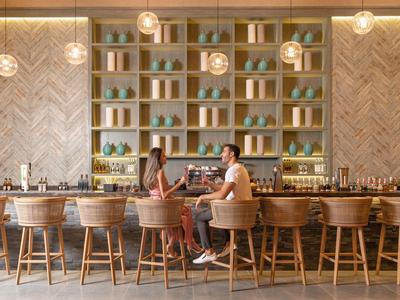 Bar moderna con sgabelli in legno e scaffali decorativi, due persone che chiacchierano.