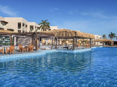 Grande piscina all'aperto con palme, ombrelloni e area salotto in un resort alberghiero sotto un cielo limpido.