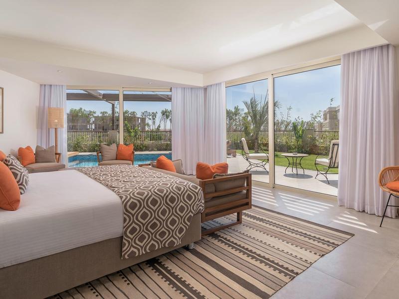 Bright hotel room with king bed, patterned linens, orange accents, and sliding glass doors to balcony.