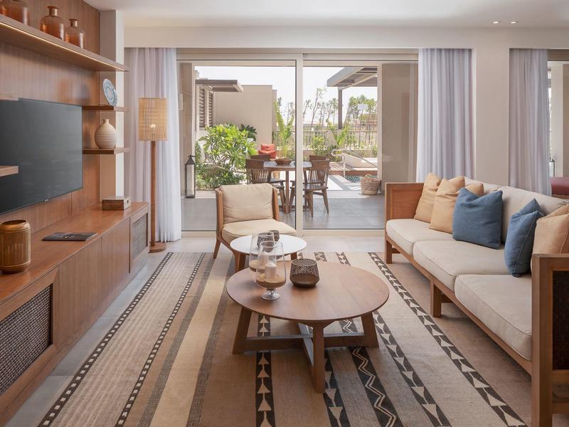 Cozy living room with wooden furniture, beige sofa, patterned rug, and a door leading to a garden patio.