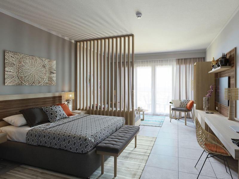 Modern hotel room with large bed, wooden partition, desk, and balcony door letting in light.