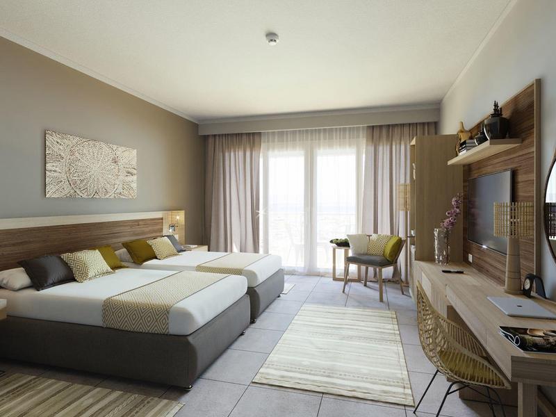 Modern hotel room with large bed, desk, armchair, and balcony access through glass doors.