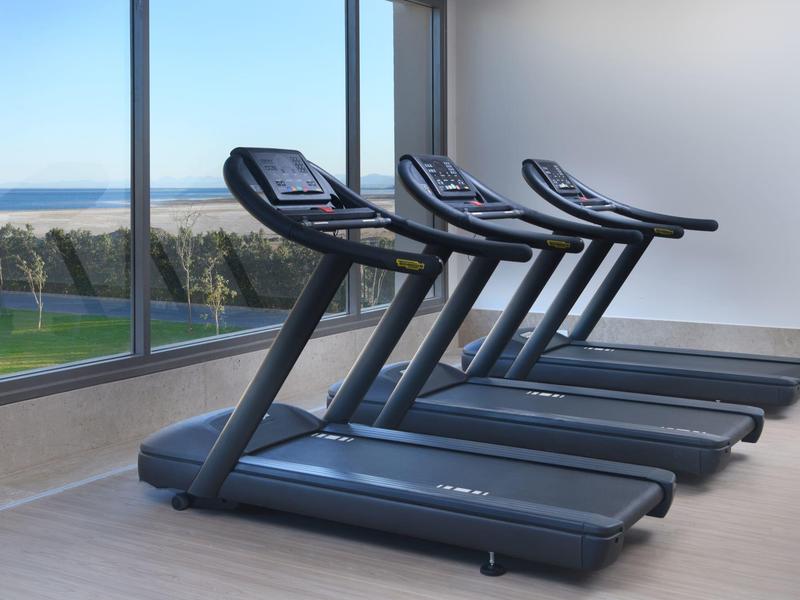 Four modern treadmills in a gym with large windows showing a green outdoor view.