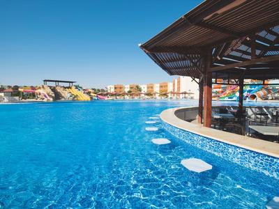 Large hotel pool with clear blue water and seating under a pavilion.