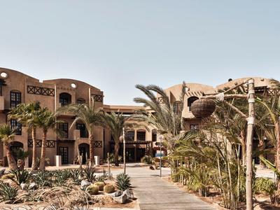 Hotel in woestijnlandschap met palmbomen en zandpad onder heldere lucht
