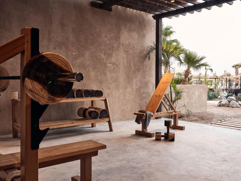 Holz-Widerstandsgeräte für Fitness in einem überdachten Außenbereich mit Blick auf Palmen und Pool.