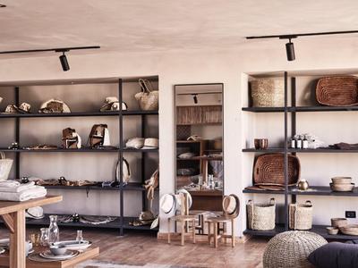 Modernes Geschäft mit Regalen voller Taschen und Accessoires, Holztisch und Hocker im Vordergrund.