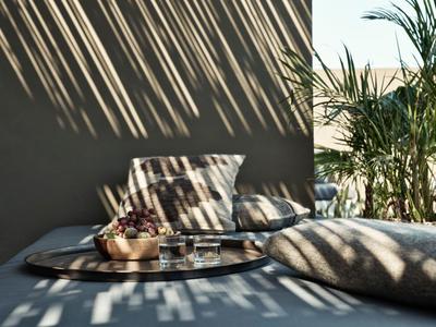 Sonnendurchflutete Terrasse mit Kissen und Pflanzen im Schattenmuster.