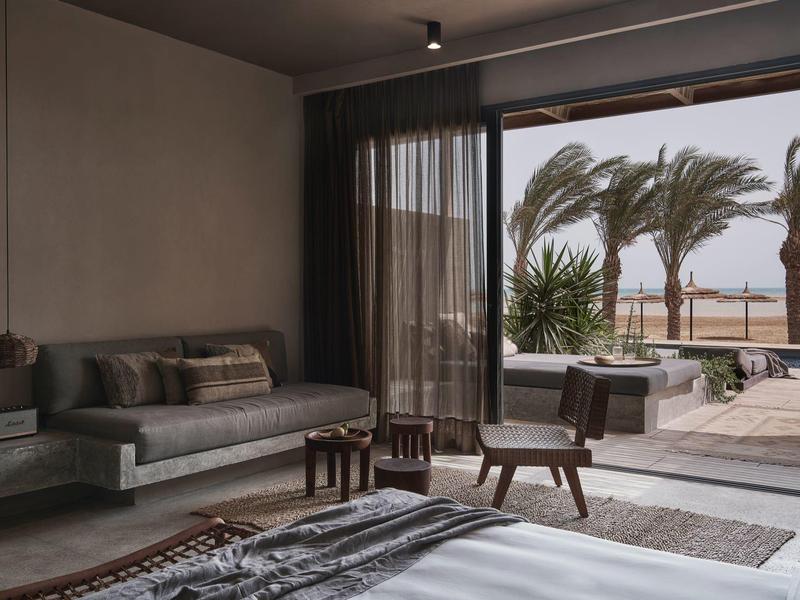 Modernes Hotelzimmer mit Terrasse, Blick auf Palmen und Meer bei Dämmerung.