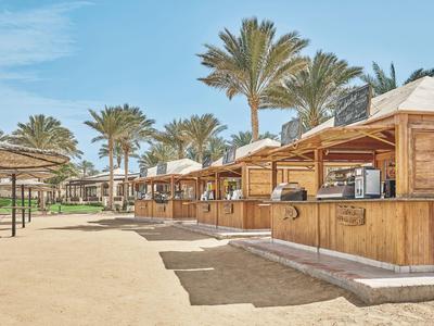 Fila di chioschi in legno con palme sullo sfondo sotto un cielo azzurro in una giornata di sole.