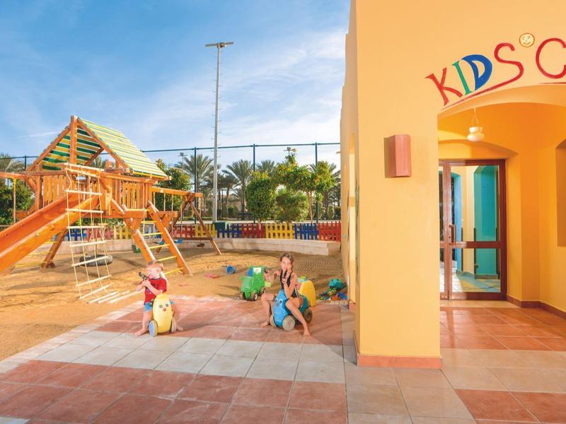 Área de juegos colorida para niños con toboganes y estructuras de escalada bajo un cielo azul en el hotel.