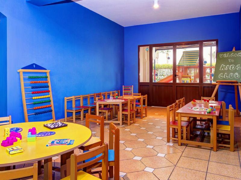 Sala de juegos para niños con mesas y sillas de colores en una habitación azul.