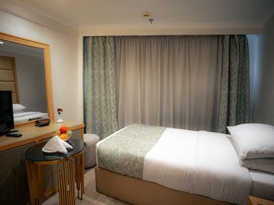 Kleine hotelkamer met een netjes opgemaakt bed, bureau met spiegel, stoel en raam met gordijnen.