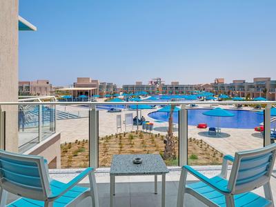 Balkonzicht op zwembad met blauwe stoelen en parasols bij een zonnig vakantieoord.