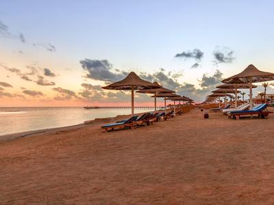 Strand met ligstoelen en parasols bij zonsondergang onder een deels bewolkte lucht.