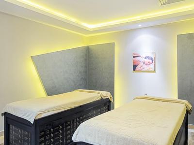 Twee massagetafels in een zacht verlichte spa kamer met grijze wandpanelen en een klein kunstwerk.