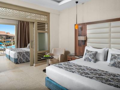 Ruime hotelkamer met kingsize bed, zithoek en schuifdeur naar balkon met uitzicht op zwembad.