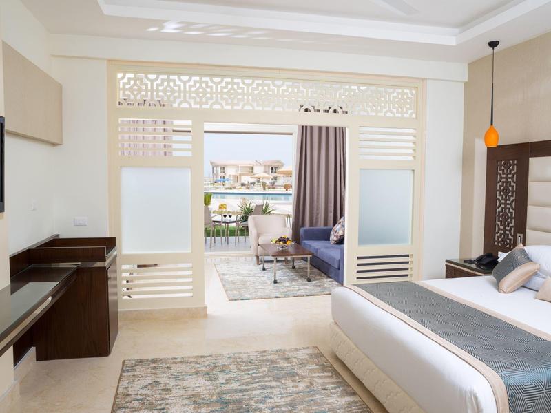 Lichte, moderne hotelkamer met bed, tv, schuifdeuren en balkon met zithoek en stadszicht.