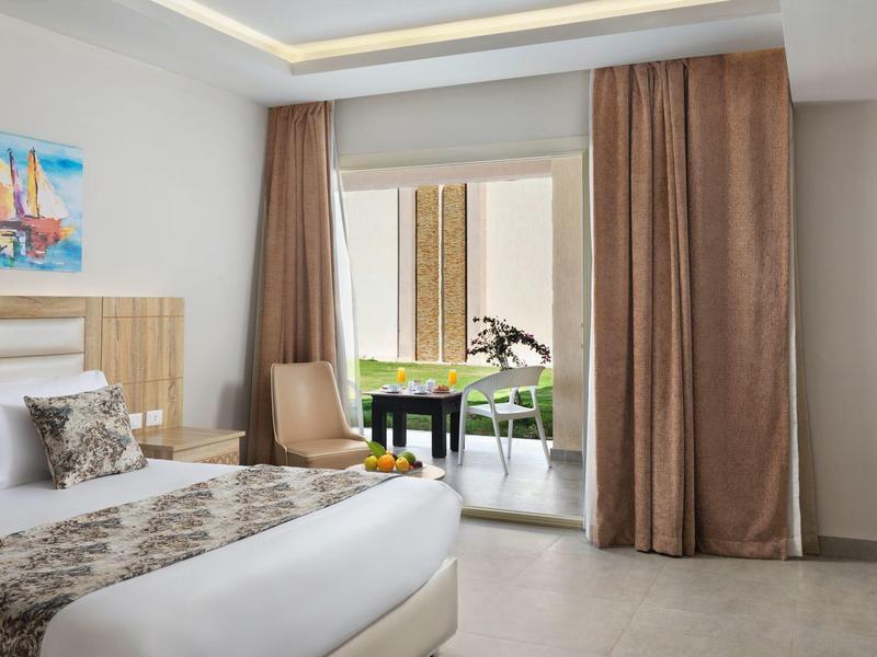 Lichte hotelkamer met een comfortabel bed, bruine gordijnen en balkonmeubilair met planten.