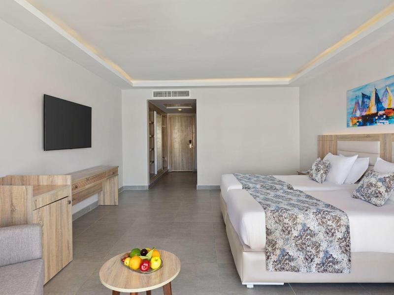 Moderne hotelkamer met twee bedden, houten meubels en een tafel met fruit.