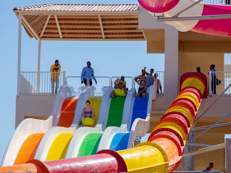 Mensen staan bovenaan kleurrijke glijbanen onder een schaduwrijke constructie in een waterpark.