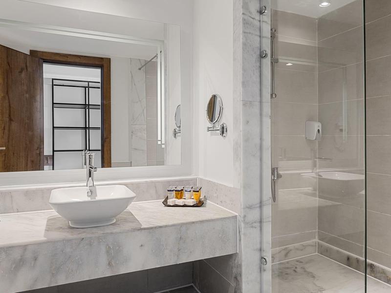 Moderne hotelbadkamer met witte wanden, grote spiegel, kommetjeswasbak en glazen douchecabine.