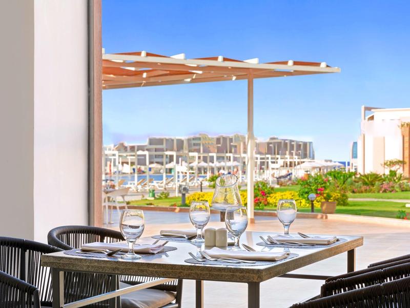 Buitentafel gedekt met glazen en borden met uitzicht op een resort en tuin onder een blauwe hemel.