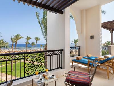Balkon mit Liegestühlen und Tisch, Blick auf Palmengarten und Meer bei klarem Himmel.