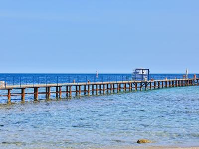 Langer Holzsteg ragt ins klare blaue Meer mit klarem Himmel im Hintergrund.